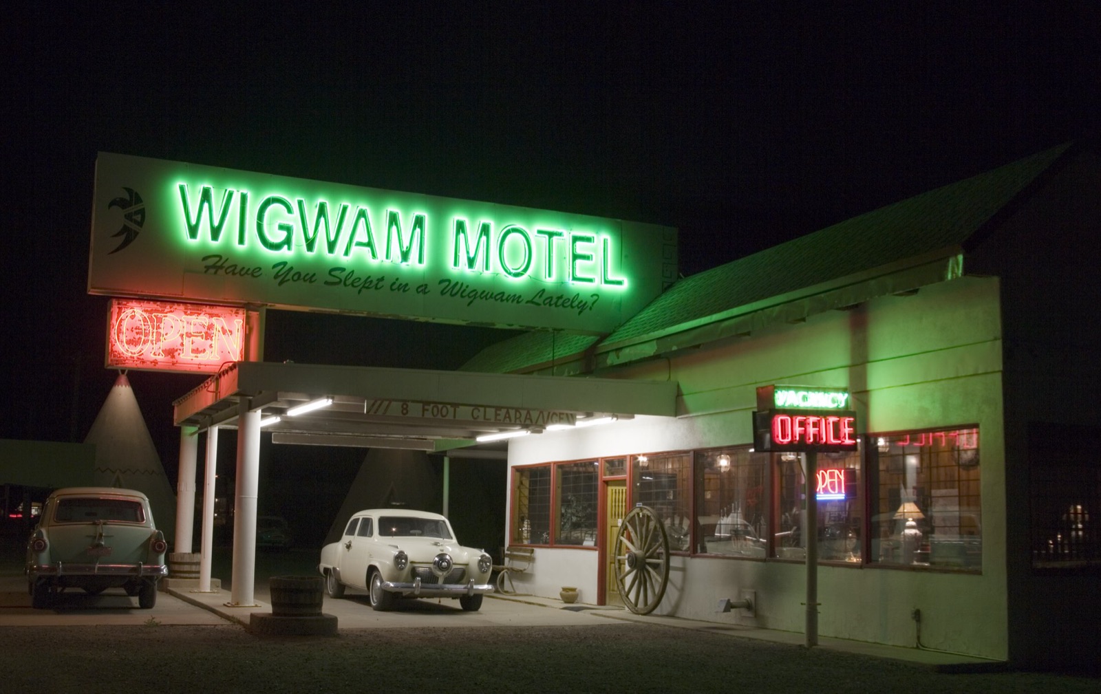 Green neon sign and office of the Wigwam Motel at night, with vintage cars and a concrete teepee, Holbrook, Arizona