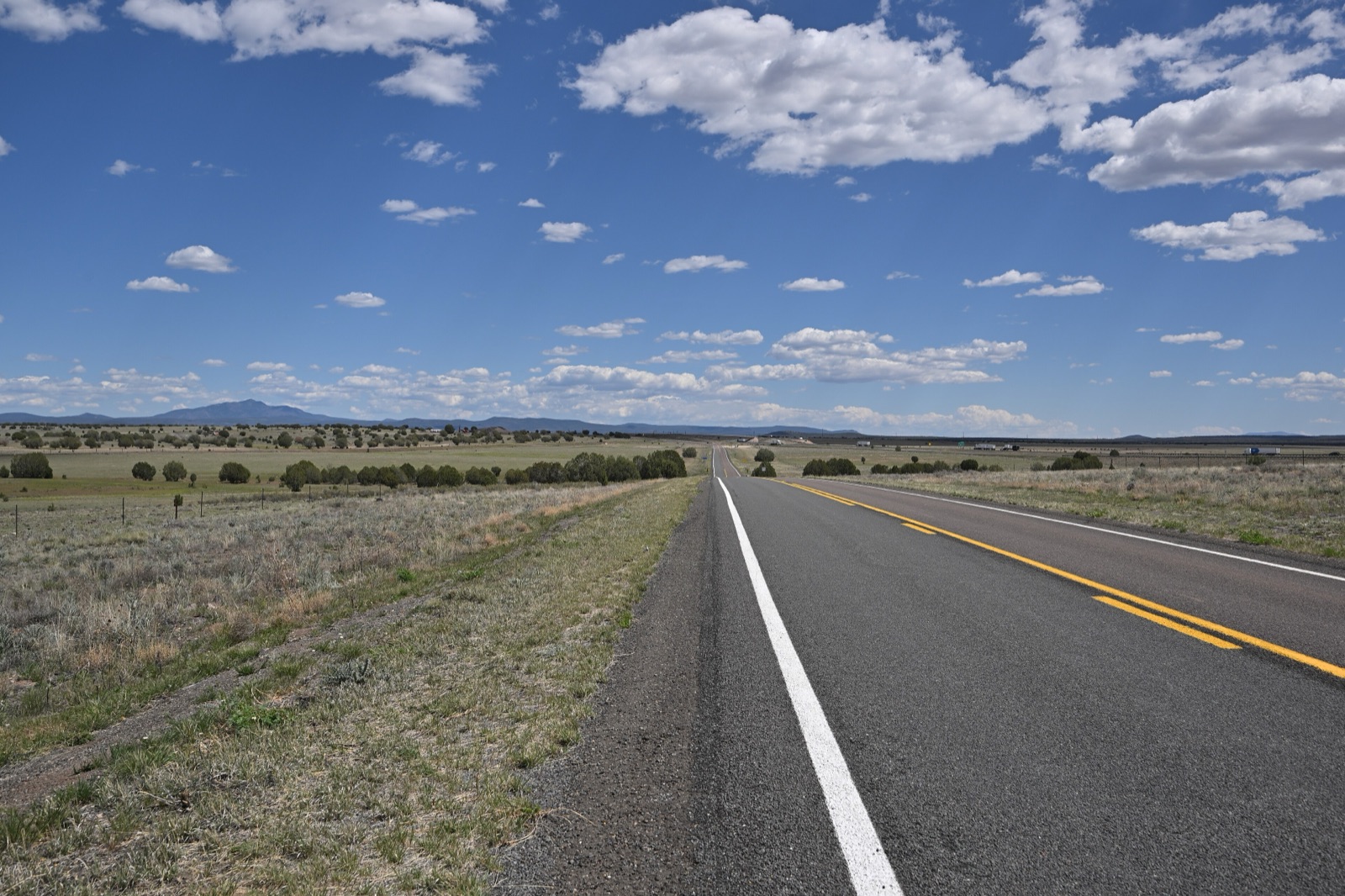 Two-lane Historic Route 66 near Crookton Road, Arizona, running straight across grassland under a blue sky with white clouds