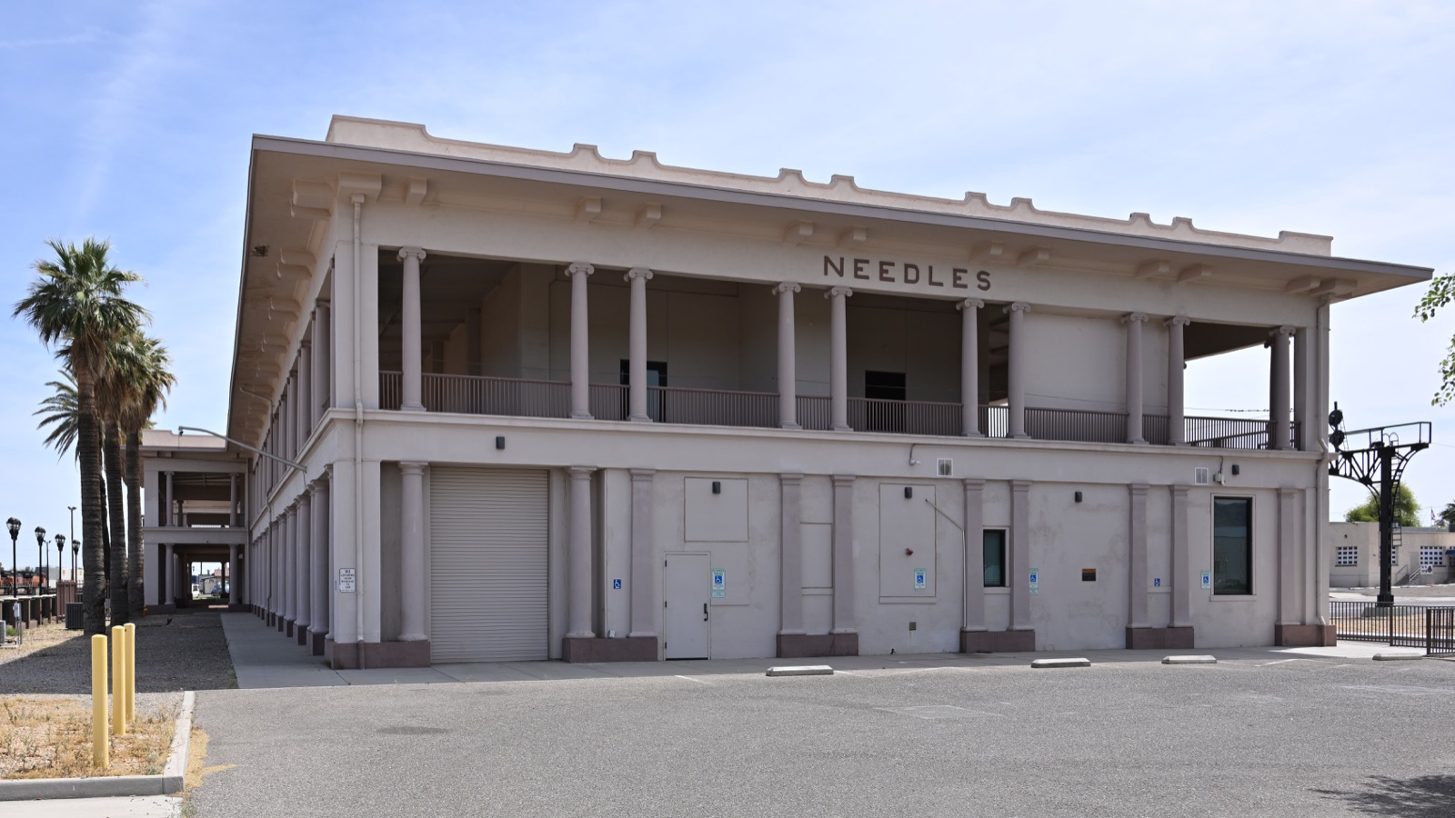 The restored El Garces Harvey House depot in Needles, California, a two-story white building with a colonnaded upper porch and NEEDLES in raised letters
