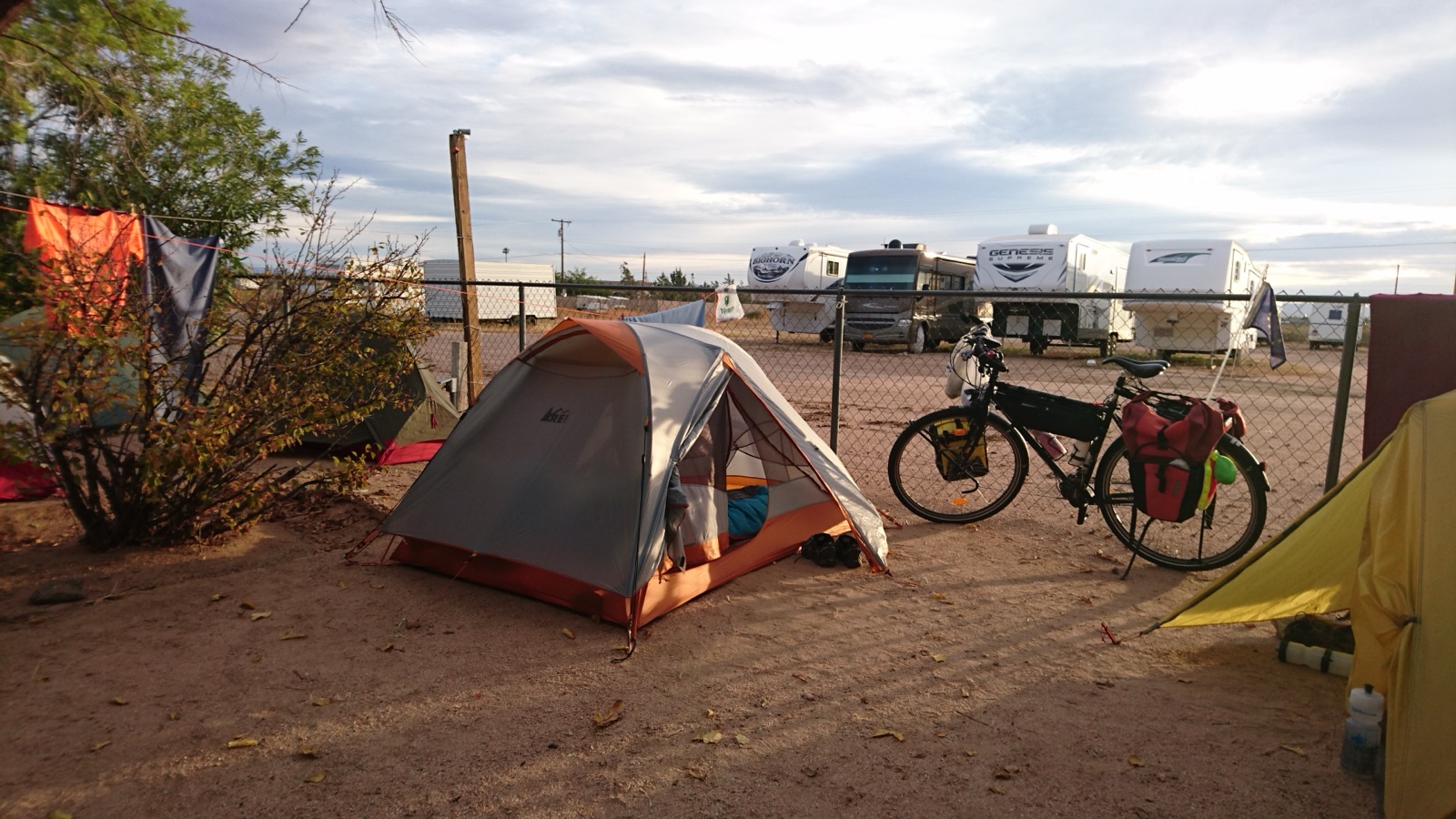 Tents and a loaded touring bicycle in the foreground with RVs and travel trailers parked behind a fence at the Kingman KOA in Arizona