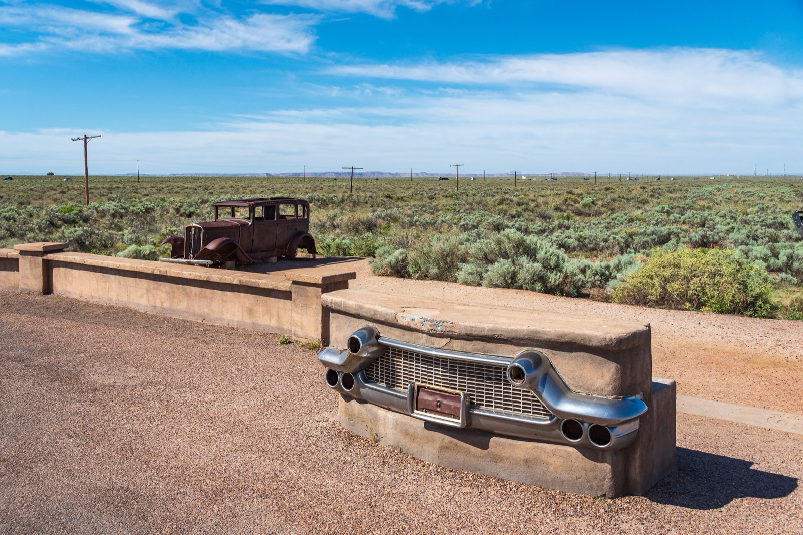 Rusted 1930s car at the Route 66 pullout in Petrified Forest National Park, with a bench shaped like a car grille and desert grassland behind