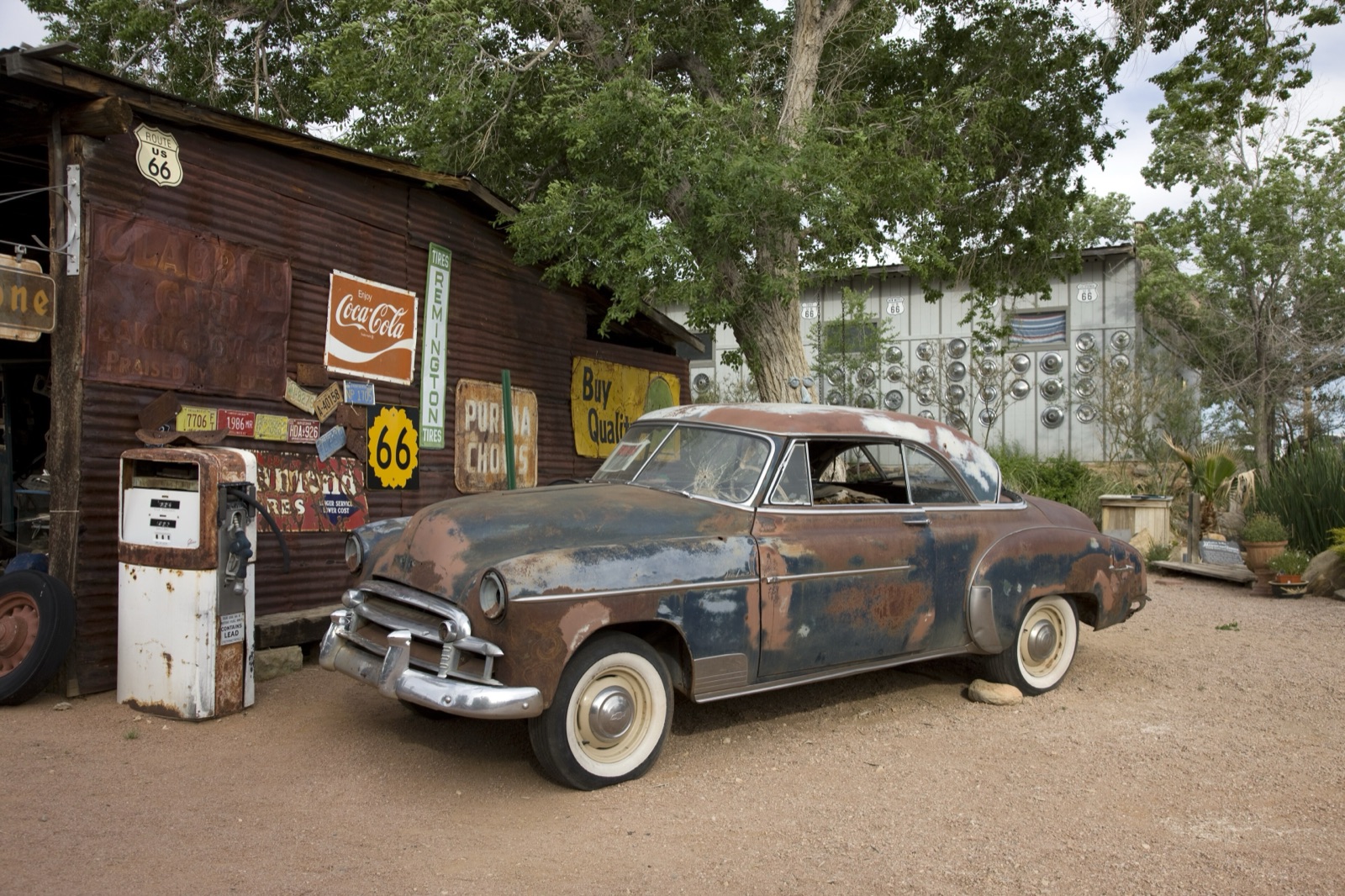 Rusted classic car and old gas pump in front of a sign-covered shed with a Route 66 shield at the Hackberry General Store, Arizona