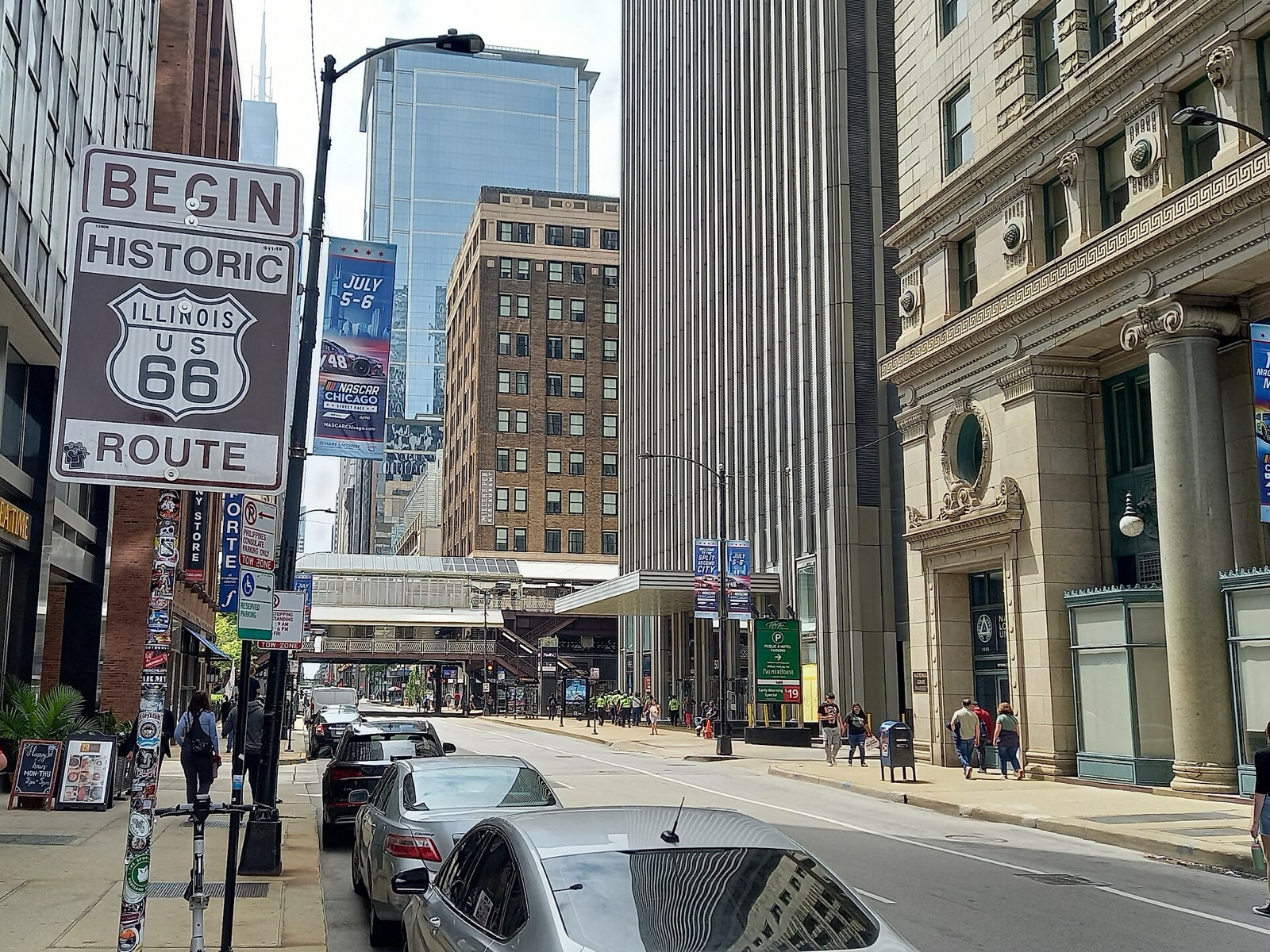 Brown Begin Historic Route 66 sign on a pole on Adams Street in downtown Chicago, with traffic and tall buildings behind it