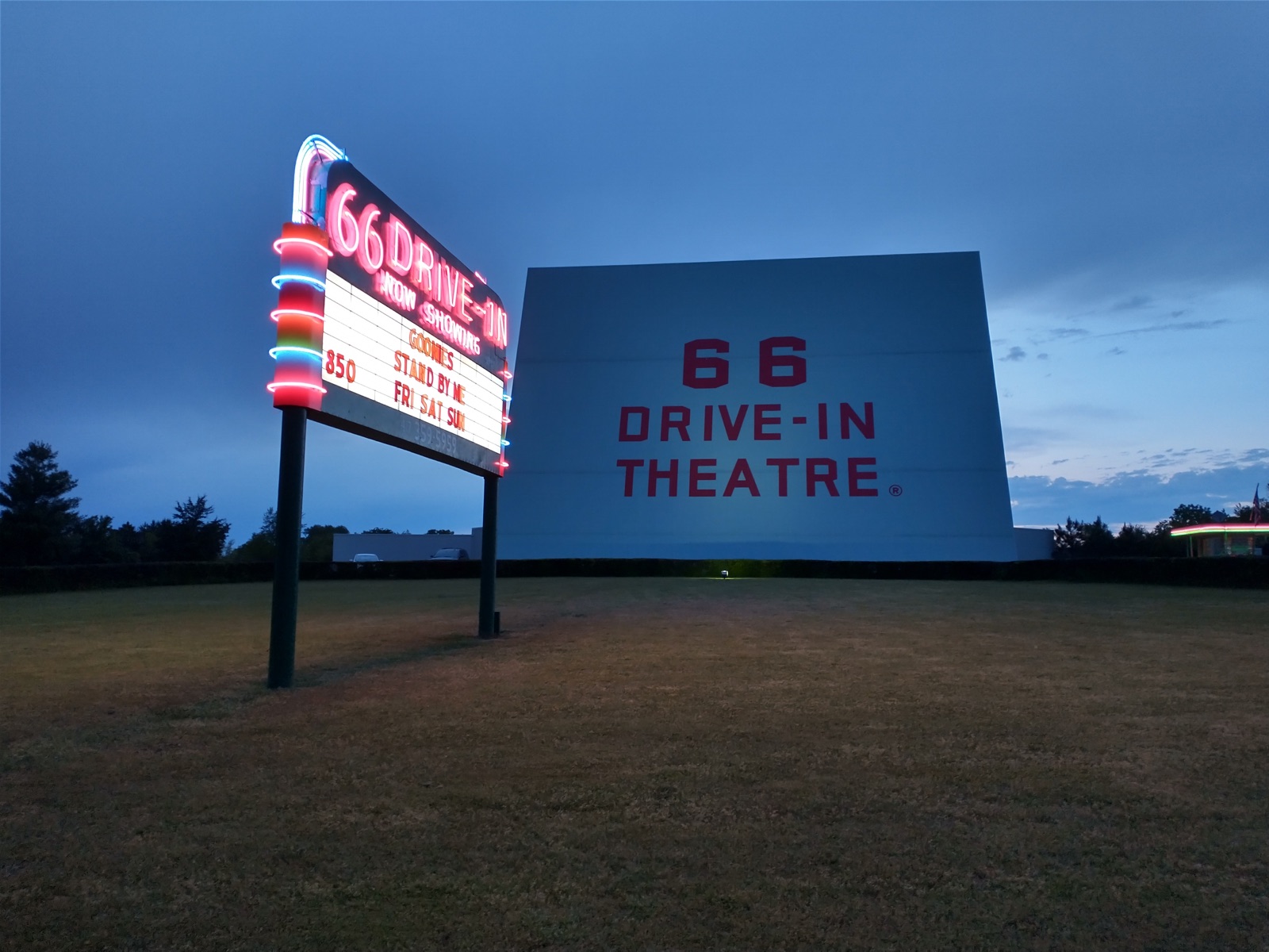 The lit neon marquee and the white screen of the 66 Drive-In Theatre in Carthage, Missouri, at twilight