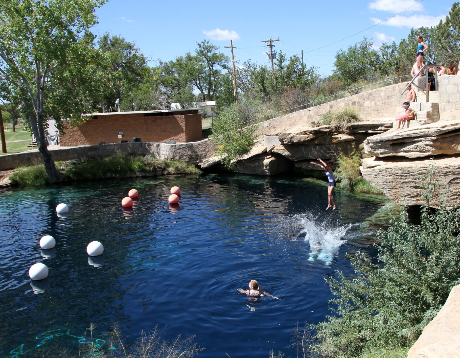 Deep blue water of the Blue Hole in Santa Rosa, New Mexico, with swimmers, marker buoys and sandstone ledges