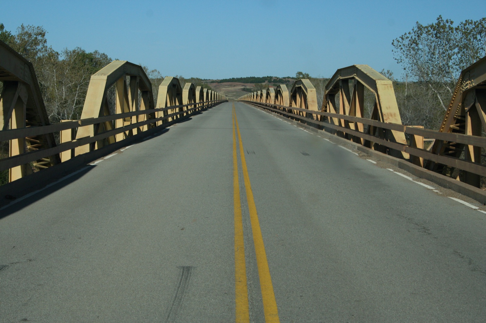 Two-lane road running between rows of yellow pony truss spans on the Bridgeport Pony Bridge over the Canadian River, Oklahoma