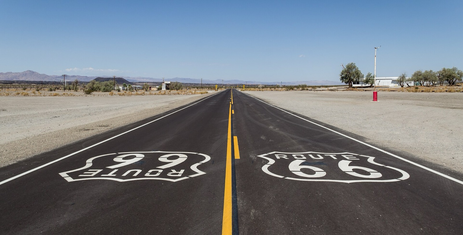 Two-lane Route 66 near Amboy, California, with Route 66 shields painted on the asphalt and desert mountains on the horizon