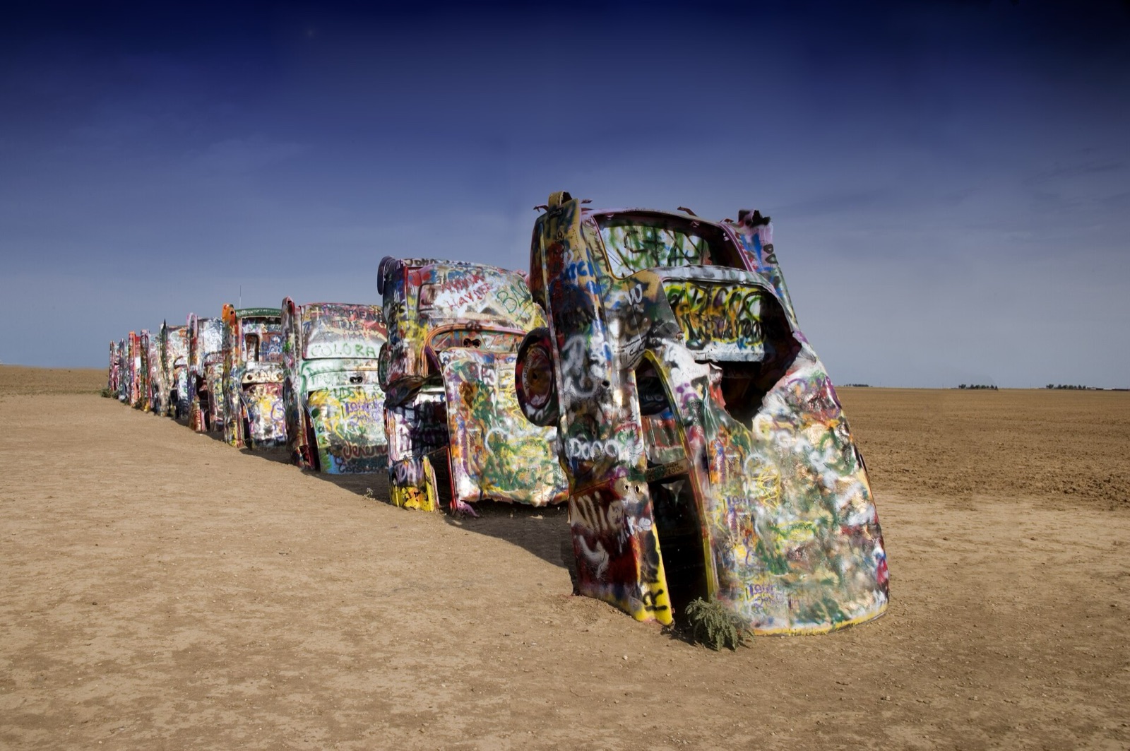A row of graffiti-covered Cadillacs buried nose-down in a dirt field at Cadillac Ranch near Amarillo