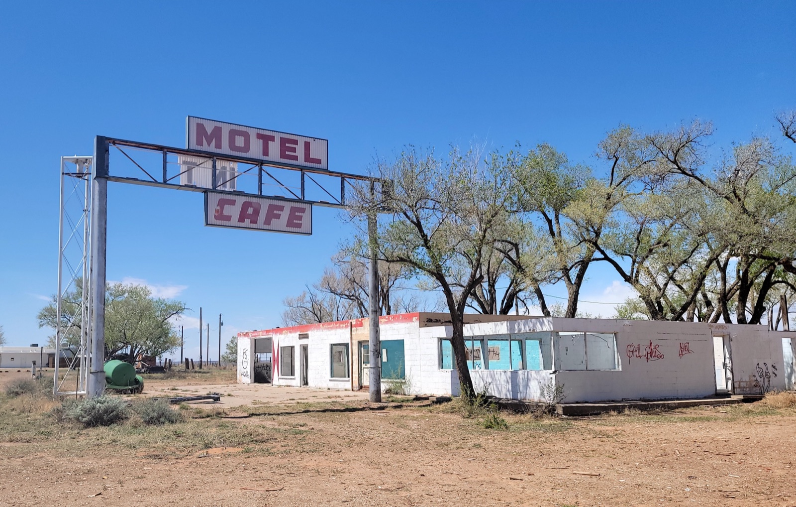 Abandoned white motel and cafe in Glenrio, Texas, under a steel arch with Motel and Cafe signs, bare trees and dry grass under a blue sky