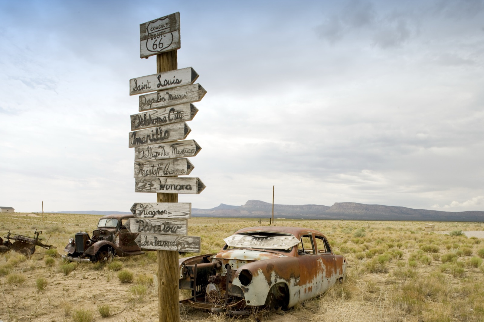 Abandoned rusted cars and a hand-painted signpost pointing to Route 66 towns in the Arizona high desert