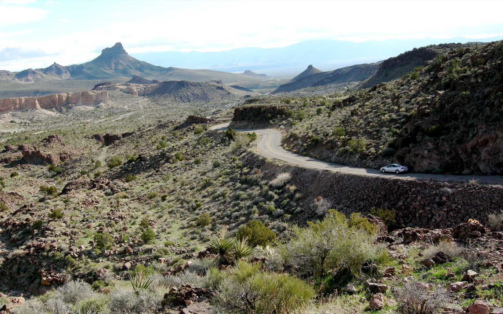 Old Route 66 curving along a hillside in the Black Mountains near Sitgreaves Pass, Arizona, with a car on the road